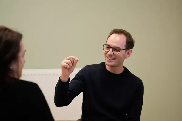 Lächelnder Mann mit Brille erklärt einer Frau etwas in einem Beratungsgespräch.